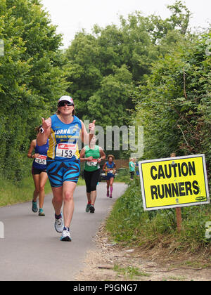 A 'caution runners' sign with female runners taking part in a road race Stock Photo