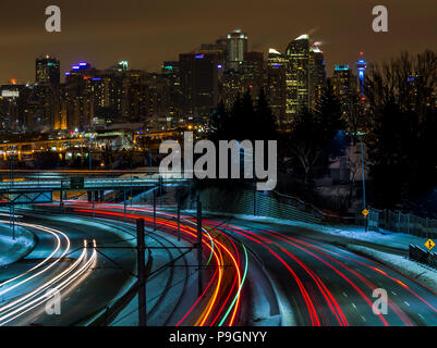 Long exposure of from the commuter trains and car traffic streaming in and out of downtown Calgary with the night skyline of the city in winter. Stock Photo