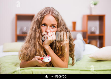 Young woman is lying in bed and watching TV. Stock Photo