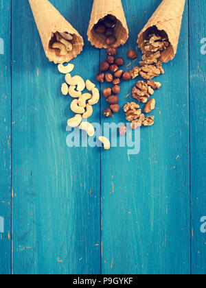 Ice cream cone with organic hazelnuts, cashews and walnuts on a blue rustic wooden table Stock Photo
