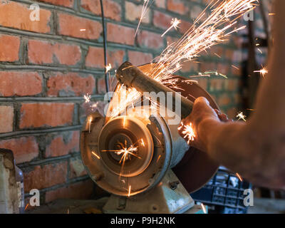 farmer sharpens a hoe on electric grindstone in rural shed Stock Photo