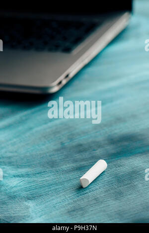 Piece of chalk on teacher's desk with laptop computer in the back Stock Photo