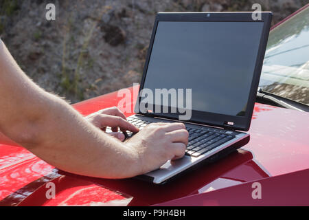 A man uses a laptop on the hood of a car Stock Photo