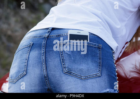 Close-up of smartphone, girl in blue denim shorts back view Stock Photo