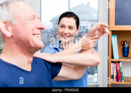 Elderly patient doing shoulder workout under assistance of therapist Stock Photo