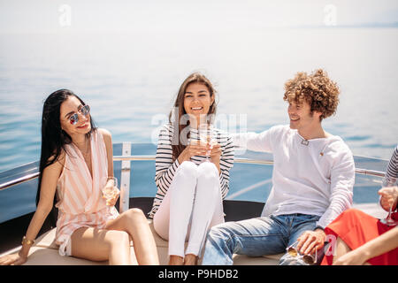 Two caucasian men invite three beautiful women to share pleasure yacht trip on the sea to islands, Young people laughing, enjoying amazing sea views Stock Photo