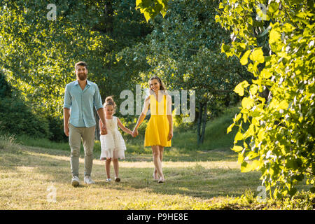 Caring parents holding hands of daughter while walking together in the park Stock Photo