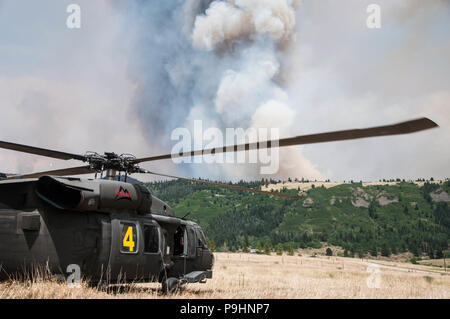A Colorado National Guard UH-60 Black Hawk crew pauses their firefighting efforts, as the airspace is cleared, while a plane drops slurry to support fire suppression efforts July 4, 2018.    Two UH-60 Black Hawk helicopter crews with aircraft, equipped with aerial water buckets, from the Chief Warrant Officer 5 David R. Carter Army Aviation Support Facility based at Buckley Air Force Base, Aurora, Colorado, depart the Spring Fire helibase, in Fort Garland, Colo., to support fire suppression efforts July 4, 2018. The team arrived and began operations July 2.    The CONG has supported the Spring Stock Photo