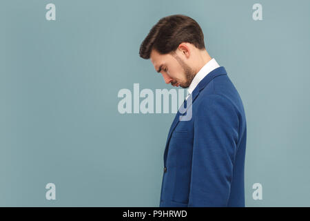 side view or profile view of sad, unhappy crying handsome bearded businessman in blue suit and white shirt. Indoor studio shot, isolated on light blue Stock Photo