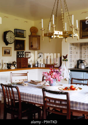 Brass light fitting above table with checked cloth in a country style kitchen with a vintage clock on the wall Stock Photo