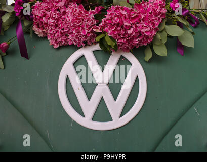 Bremen, Germany - July 17th, 2018 - Close-up photo of the front of a green VW T3 van with white VW logo decorated with pink flowers Stock Photo