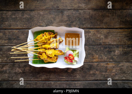 top view delicious pork satay skewers with peanut dipping suace and sider in white paper box on wooden table, one of famous street food Thai local dis Stock Photo