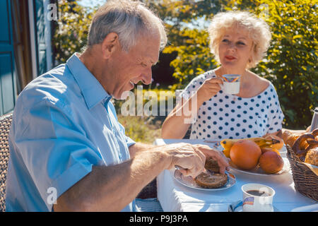 Senior woman and man having breakfast sitting in their garden Stock Photo