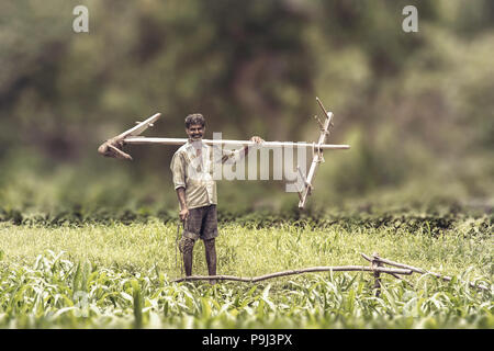 Happy Indian farmer standing with wooden plough in rice field Stock Photo