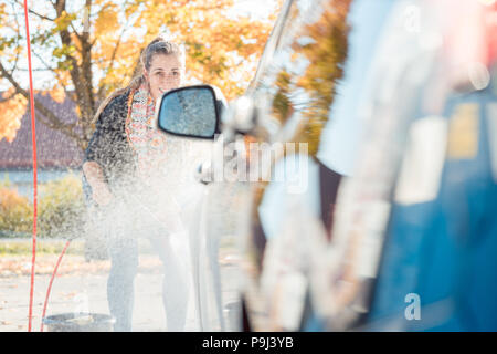 Woman using high pressure nozzle to clean her car Stock Photo