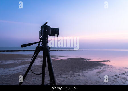 Dslr digital professional camera stand on tripod photographing sea, twilight sky and cloud landscape. photographer shoots video of the sunrise in the  Stock Photo