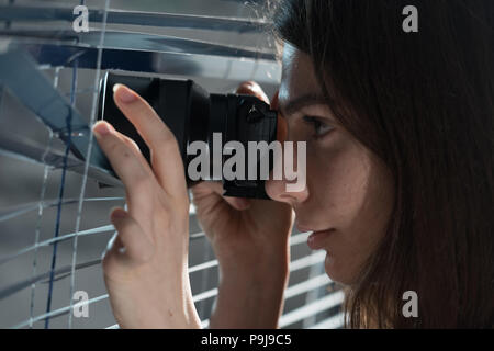 Young woman Paparazzi take a photo suspiciously from around a blinds  while using a camera. GDPR Concept Stock Photo