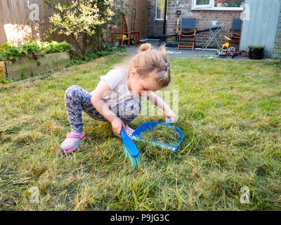 Three year old girl sweeping up cut grass in the back garden, London, UK Stock Photo