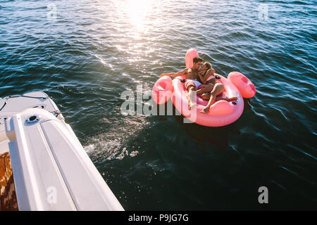 Romantic young couple relaxing on inflatable top in sea tied with a yacht. Man and woman enjoying on summer vacation. Stock Photo