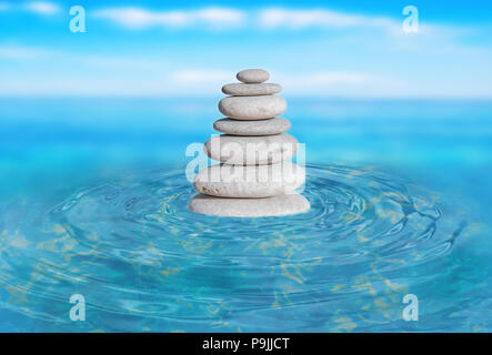Zen stones stack from large to small in water with circular waves and blured sky Stock Photo