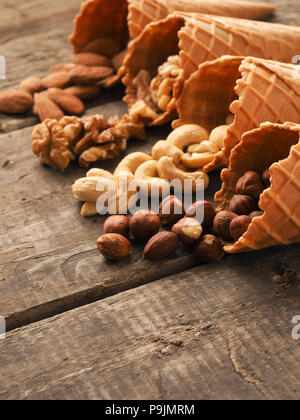 Ice cream cone with organic almonds, hazelnuts, cashews and walnuts on a rustic wooden table Stock Photo