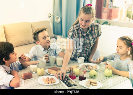 Girls and boys talking with cups of tea and sweet pie and jam at home Stock Photo
