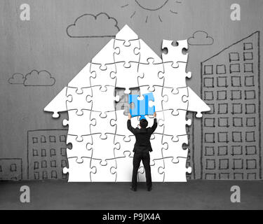Putting last blue puzzles in house shape on concrete wall Stock Photo