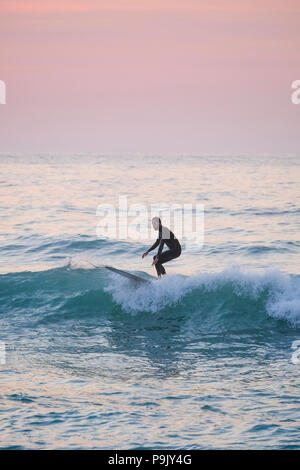 Surfer off Porthmeor Beach at St Ives in Cornwall as the sun goes down Stock Photo