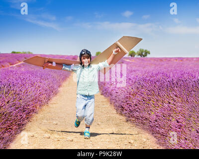 Portrait of happy boy running through lavender field and waving cardboard wings trying to fly Stock Photo