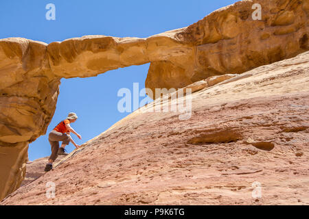 WADI RUM DESERT, JORDAN - APRIL 30, 2016: Woman climbing to the Burdah rock bridge in Wadi Rum desert - Valley of the Moon in Jordan. UNESCO World Her Stock Photo