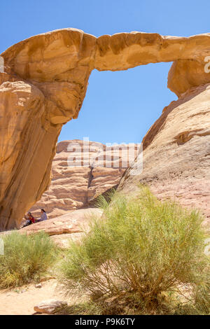 WADI RUM DESERT, JORDAN - APRIL 30, 2016: People resting under the Burdah rock bridge in Wadi Rum desert - Valley of the Moon in Jordan. UNESCO World  Stock Photo