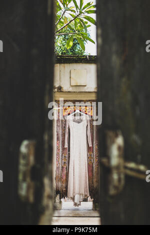 Chic wedding dress hanging on door of traditional balinese villa Stock Photo