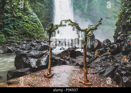 Tropical wedding ceremony with waterfall view in jungle canyon. Decorated with green ivy, old branches and hanging lamps Stock Photo