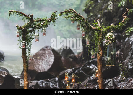 Tropical wedding ceremony with waterfall view in jungle canyon. Decorated with green ivy, old branches and hanging lamps Stock Photo