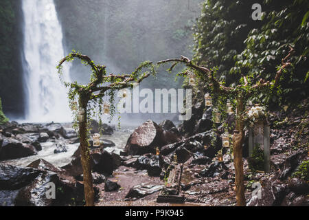 Tropical wedding ceremony with waterfall view in jungle canyon. Decorated with green ivy, old branches and hanging lamps Stock Photo