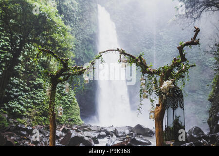 Tropical wedding ceremony with waterfall view in jungle canyon. Decorated with green ivy, old branches and hanging lamps Stock Photo
