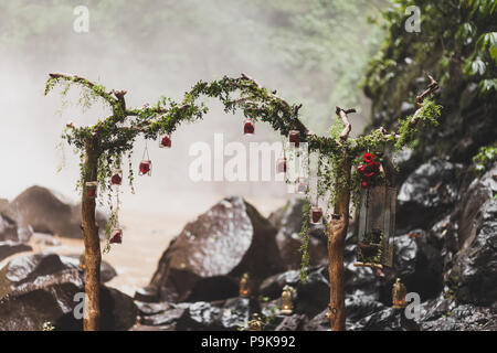 Tropical wedding ceremony with waterfall view in jungle canyon. Decorated with green ivy, old branches and hanging lamps Stock Photo