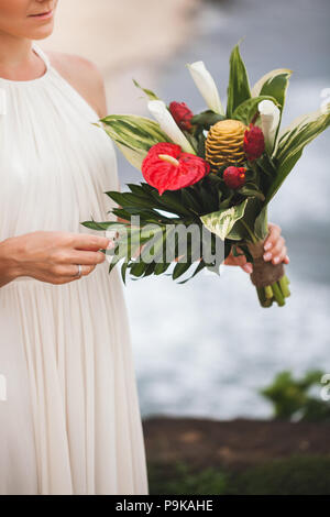 Bouquet with red and green tropical flowers in bride's hands Stock Photo