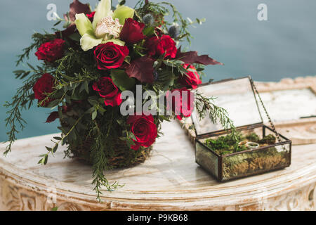 Wedding ceremony reception table with bouquet in Boho style. Decorated with red roses, yellow orchid. Box with rings Stock Photo