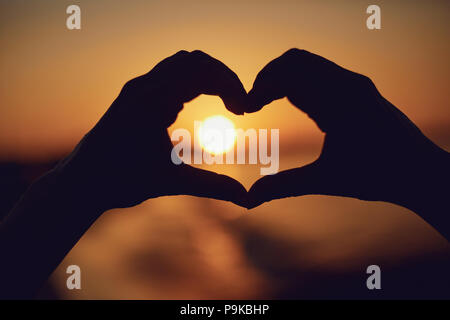 Hands in the shape of heart on the sunset by the sea. Stock Photo