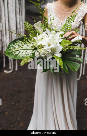 Bride holding in hands huge green bouquet with tropical leaves and flowers Stock Photo