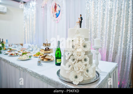 Close-up photo of big white wedding cake decorated with fondant flowers and two figures on top. Stock Photo