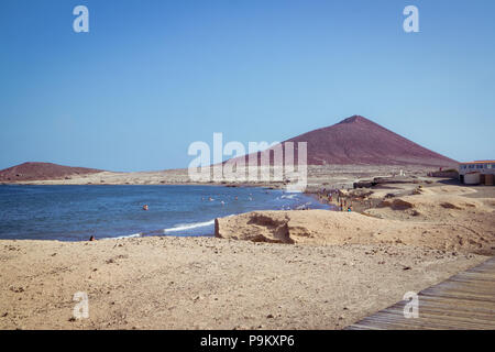 Playa El Médano beach and bay with tourists, the Atlantic Ocean and the Red Mountain (La Montaña Roja) in Tenerife - South Coast Stock Photo