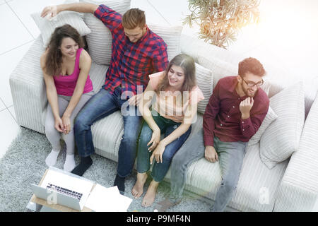 triumphant group of friends laughing while sitting on the couch in the living room Stock Photo