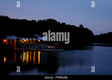 Lights of the boathouse reflected in the water during the early morning twilight at Lake Johnson in Raleigh North Carolina Stock Photo