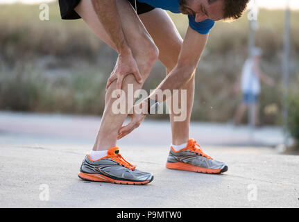 close up of runner touching painful twisted or broken ankle shin or