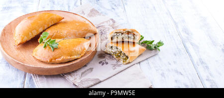 Fresh homemade pies with cheese and greens for breakfast. Portion pies. On a wooden plate and on a white background. Free space for text or advertising Stock Photo