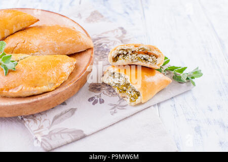 Fresh homemade pies with cheese and greens for breakfast. Portion pies. On a wooden plate and on a white background. Free space for text or advertising Stock Photo