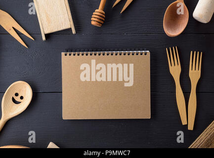 open notebook with blank pages in the middle of wooden kitchen items on a black table Stock Photo