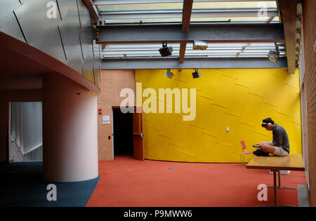 A young man with headphones on, sitting on the table in the Ray and Maria Stata Center in MIT Stock Photo